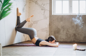 A young women with knees on wall as she lay on stomach to stretch after yoga class.