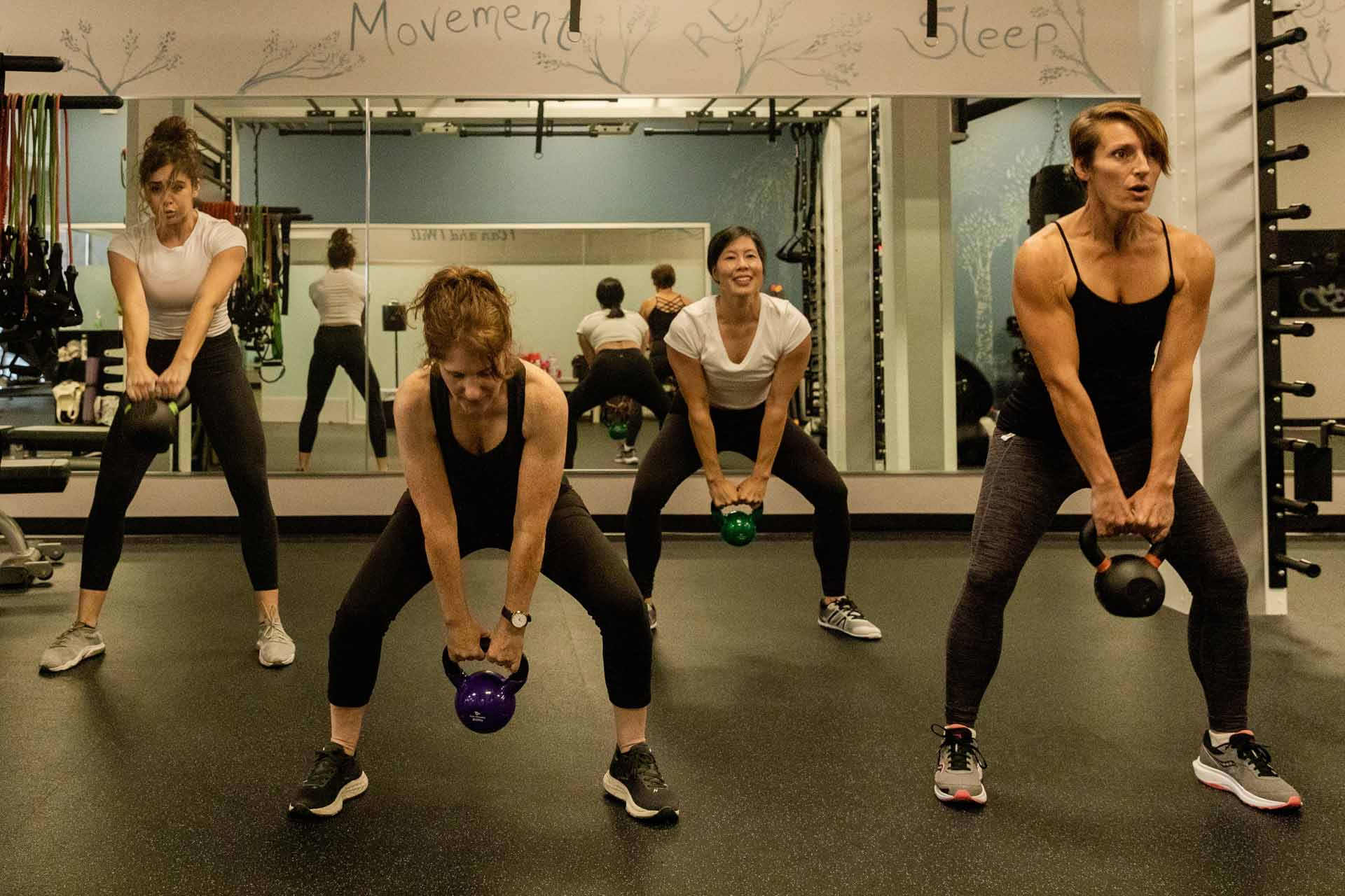 A group of students in a personal training session work to list heavy weights.