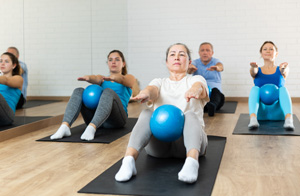 Elderly woman practicing pilates with ball in gym area.
