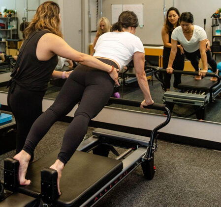 A Pilates instructor assisting a student on a Pilates Reformer machine to ensure proper positioning during a private personal training session.