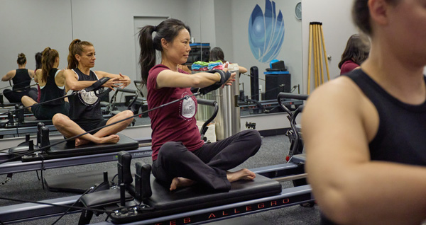 A group in a Pilates class using resistance from a Pilates reformer to build muscle.