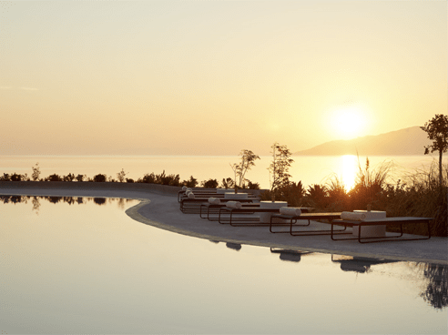 Sun setting in the distance with a pool in the foreground at the Paros Island Greece Retreat.