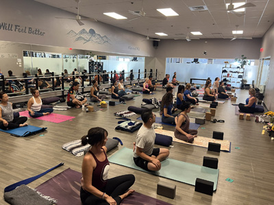 Students sitting on yoga mats facing the instructor teaching them next pose.