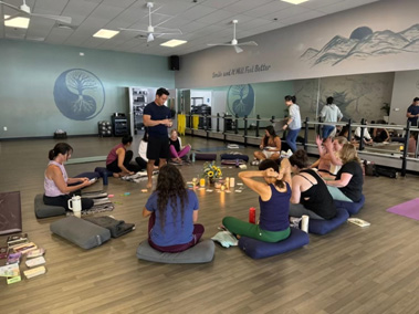 Yoga students sit in a circle as the yoga instructor speaks.