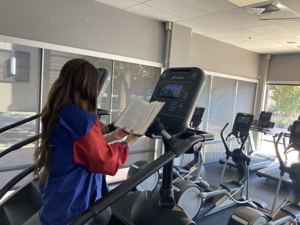 a well studio student getting in her cardio on an elliptical machine and reading at the same time