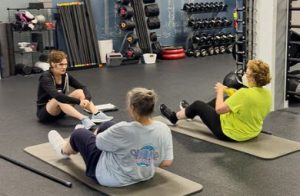 Two women on the ground doing strength training exercises while their personal training coaches them.